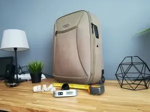 A green suitcase next to a luggage scale and measuring tape