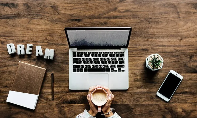 Top view of a laptop, phone, notebook and a coffe on a wooden desk