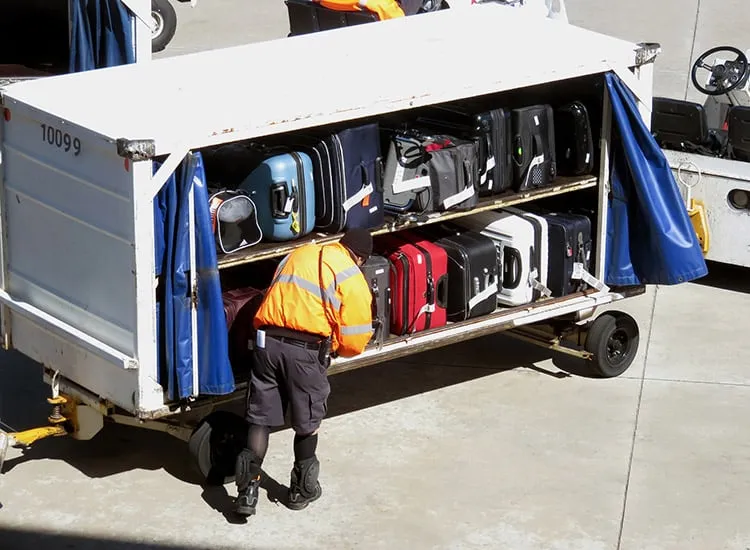 a baggage handler unloading checked luggage from an airport truck