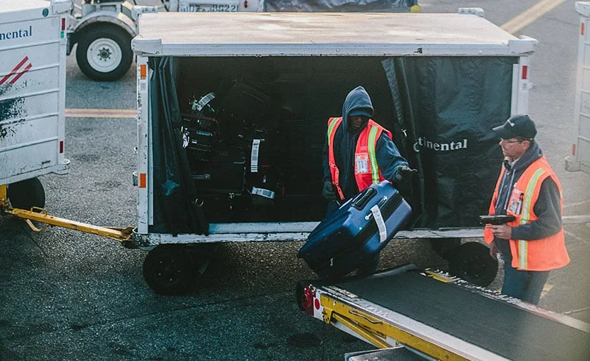 Baggage handlers loading checked luggage in airplane
