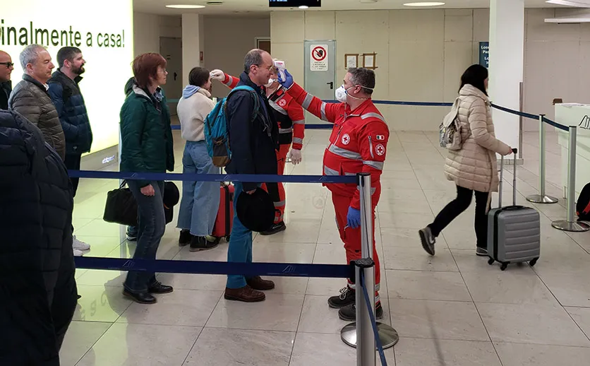 Airport employee checking temperature of passengers at security