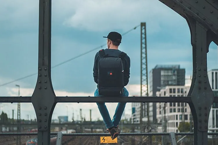 a man sitting on a metal ledge with a black laptop backpack