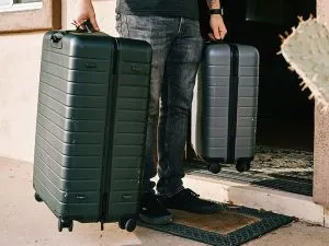 A man holding a large checked suitcase and a smaller carry-on