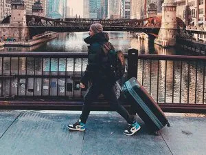 A man walking with a checked suitcase in a large city