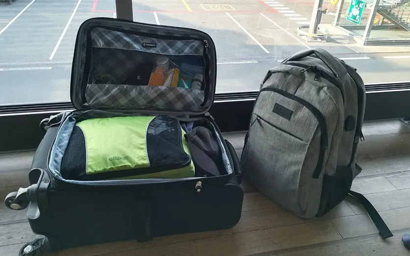 An open carry-on suitcase next to a backpack in airport